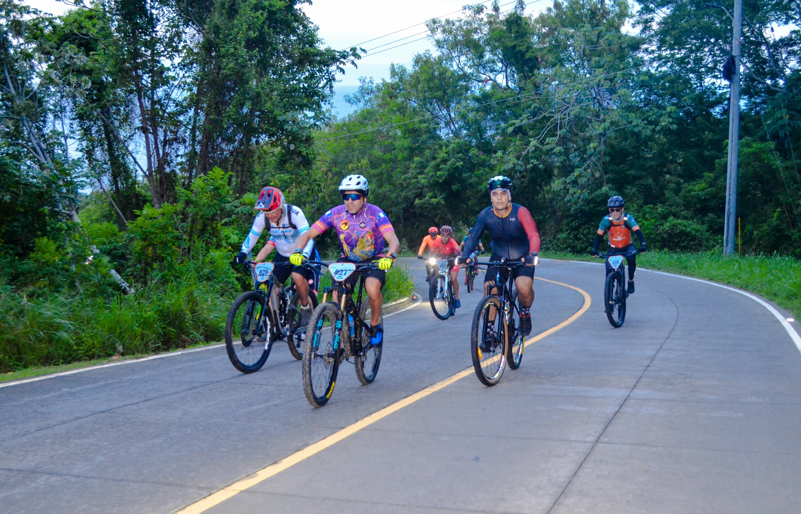 Roatán Point 2 Point — grupo ciclistas carretera curva bosque. Fotografía Adonis Maradiaga.